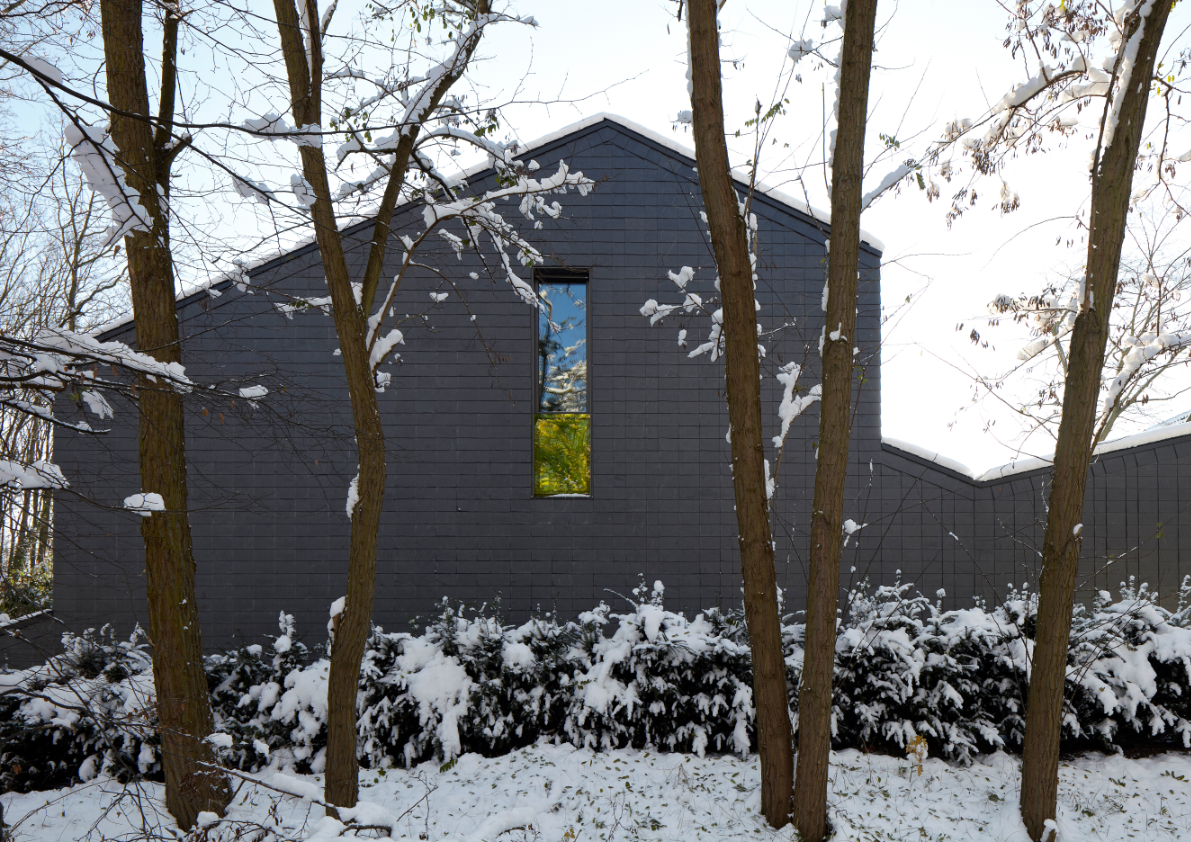 Schwarzer Baukörper mit Schindelfassade und verschneite Baumlandschaft