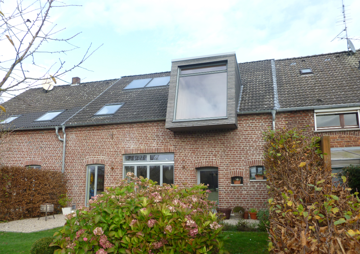 Wohnhaus mit Ziegel- und Holzfassade in winterlicher Landschaft zwischen Bäumen und Blick auf den See mit einer grossen Fenstergaube