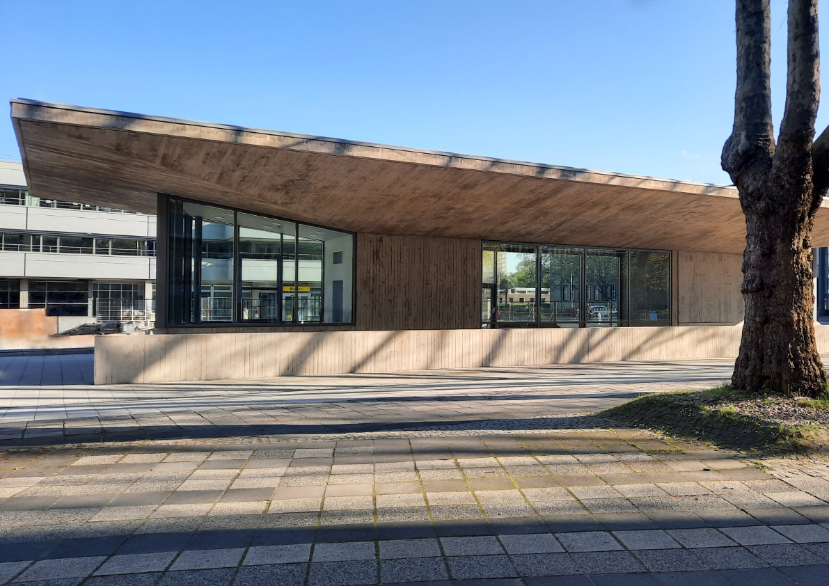 Skulpturales Gebäude mit weit auskragendem Dach im städtischen und denkmalgeschützten Umfeld dem Albertus-Magnus-Platz Universität Köln