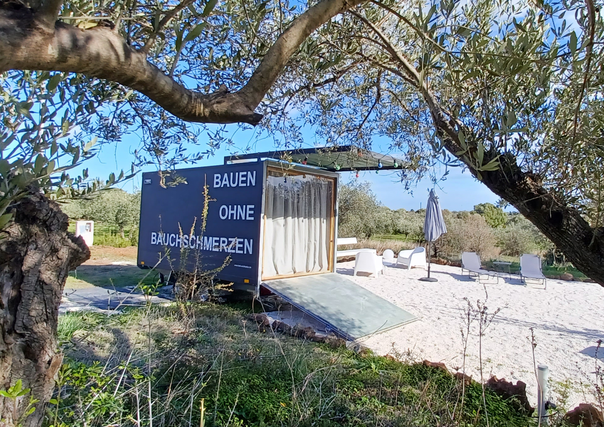 Tiny-Haus in ländlicher Umgebung zwischen Olivenbäumen und Sitzbereichen im Freien.